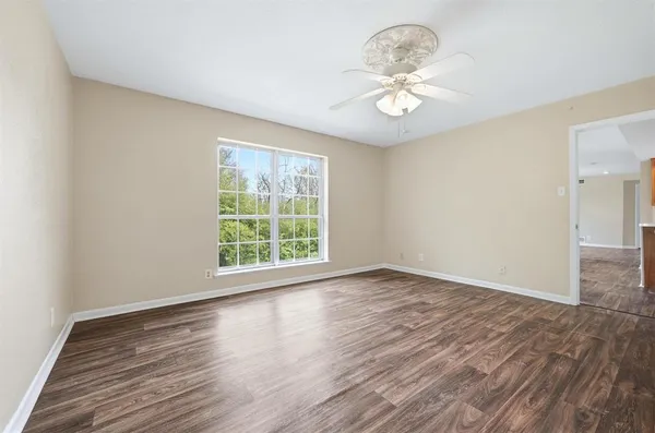 an empty room with wooden floor chandelier fan and windows