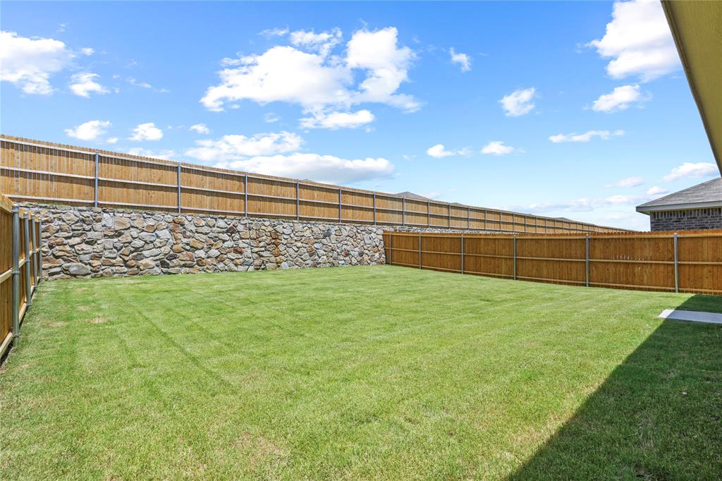 1138 Barbary Flds Street Forney, TX 75126 - Photo 25 of 25 Expansive backyard featuring a manicured lawn, full privacy fencing, and a stone retaining wall