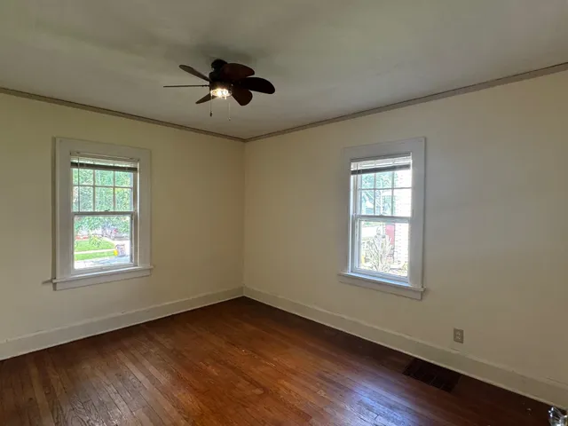 an empty room with wooden floor ceiling fan and windows