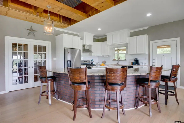 a kitchen with stainless steel appliances kitchen island granite countertop a dining table chairs and a refrigerator