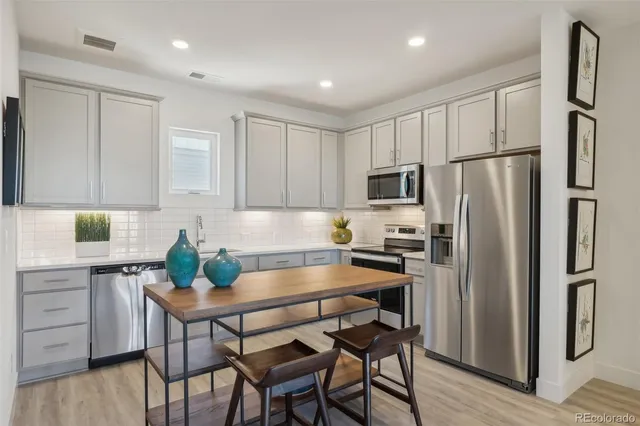a kitchen with stainless steel appliances a dining table chairs refrigerator and microwave