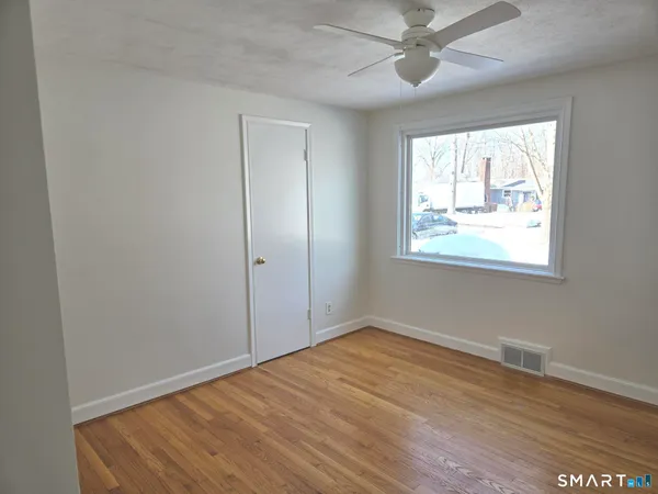 an empty room with wooden floor fan and windows