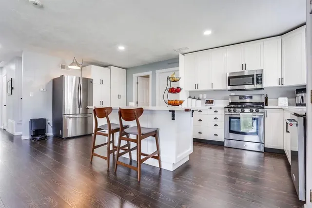 a kitchen with stainless steel appliances a refrigerator a stove top oven a sink dishwasher and white cabinets with wooden floor