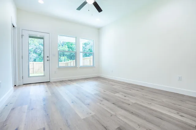an empty room with wooden floor fan and windows