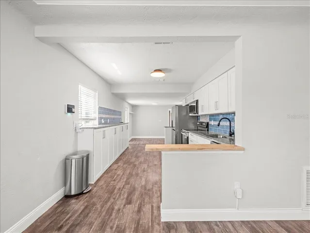 a room with stainless steel appliances kitchen island granite countertop a refrigerator a stove and a sink with wooden floor