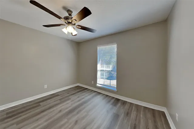 an empty room with wooden floor ceiling fan and windows