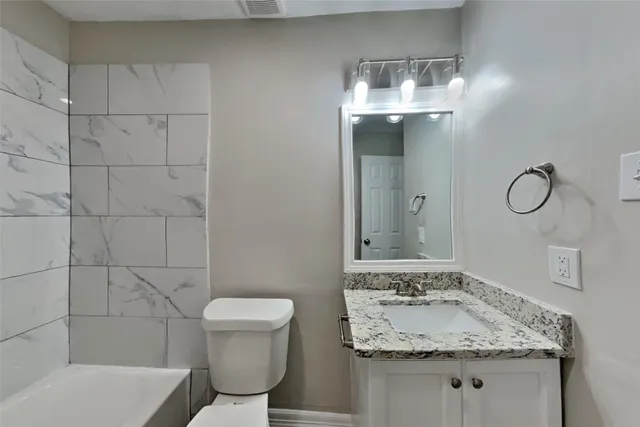 a bathroom with a granite countertop sink a toilet and mirror