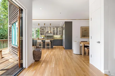 a living room with stainless steel appliances furniture wooden floor and a kitchen view