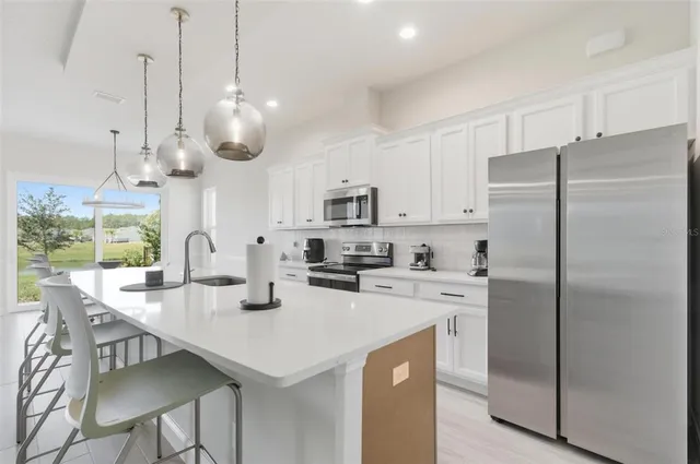 a kitchen with stainless steel appliances granite countertop a refrigerator a sink dishwasher a stove a dining table and chairs with wooden floor
