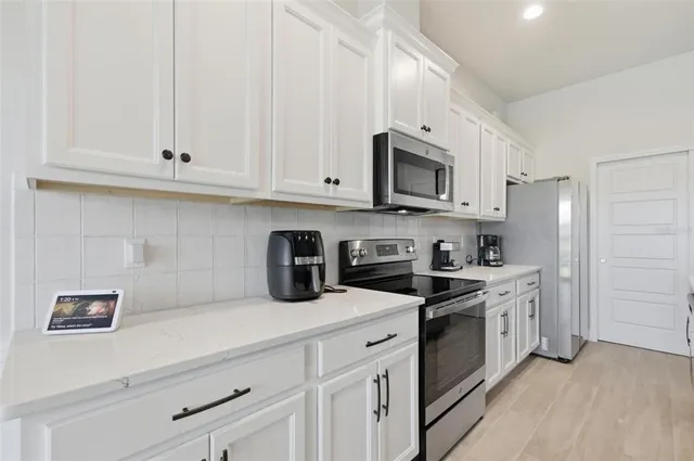 a kitchen with stainless steel appliances granite countertop white cabinets a sink a stove a microwave and a refrigerator