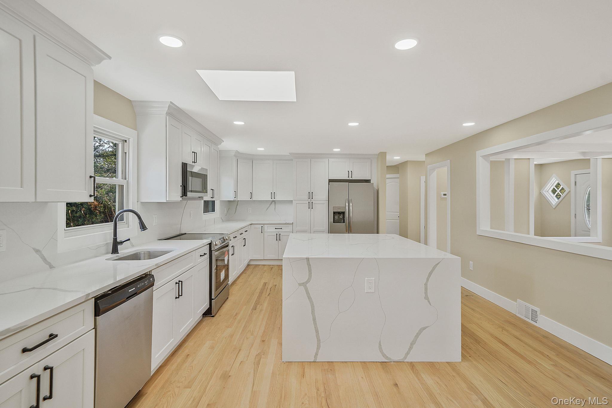 48 Vernon Street Patchogue, NY 11772 - Photo 6 of 31 Kitchen with stainless steel appliances, a skylight, white cabinets, light stone countertops, and a center island
