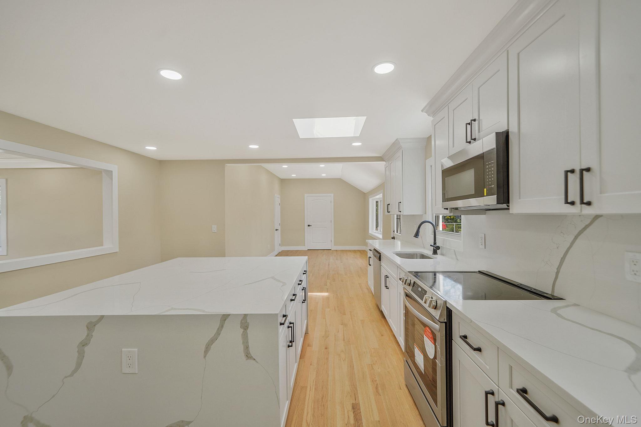 48 Vernon Street Patchogue, NY 11772 - Photo 8 of 31 Kitchen with a skylight, appliances with stainless steel finishes, light stone counters, light wood-style flooring, and recessed lighting