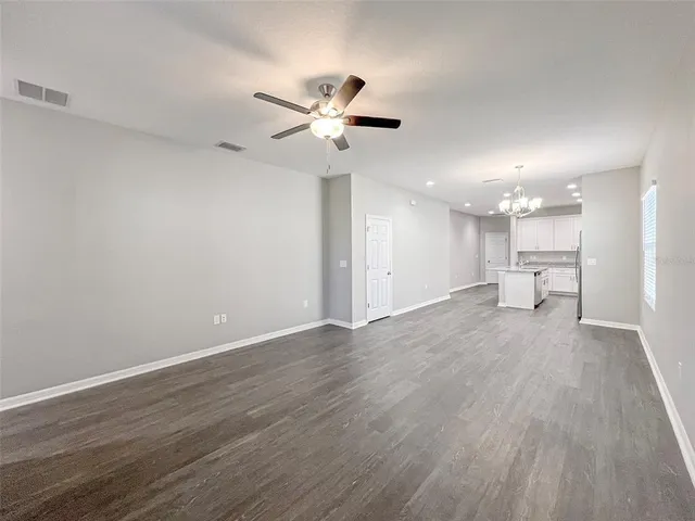 a view of an empty room with a kitchen and a ceiling fan