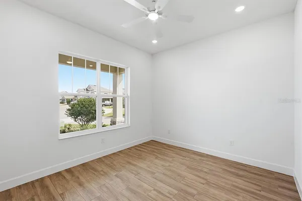 an empty room with wooden floor ceiling fan and windows