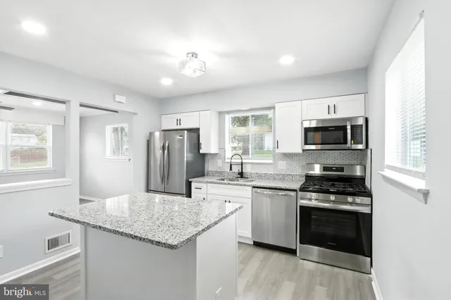 a kitchen with stainless steel appliances granite countertop a stove top oven a sink dishwasher a refrigerator and a dining table with wooden floor