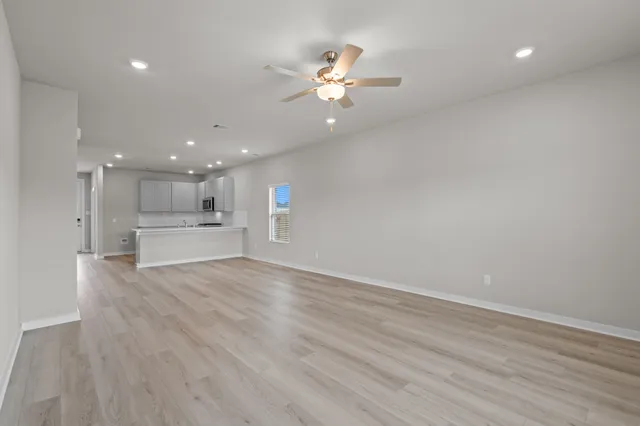 a view of an empty room with wooden floor and a kitchen