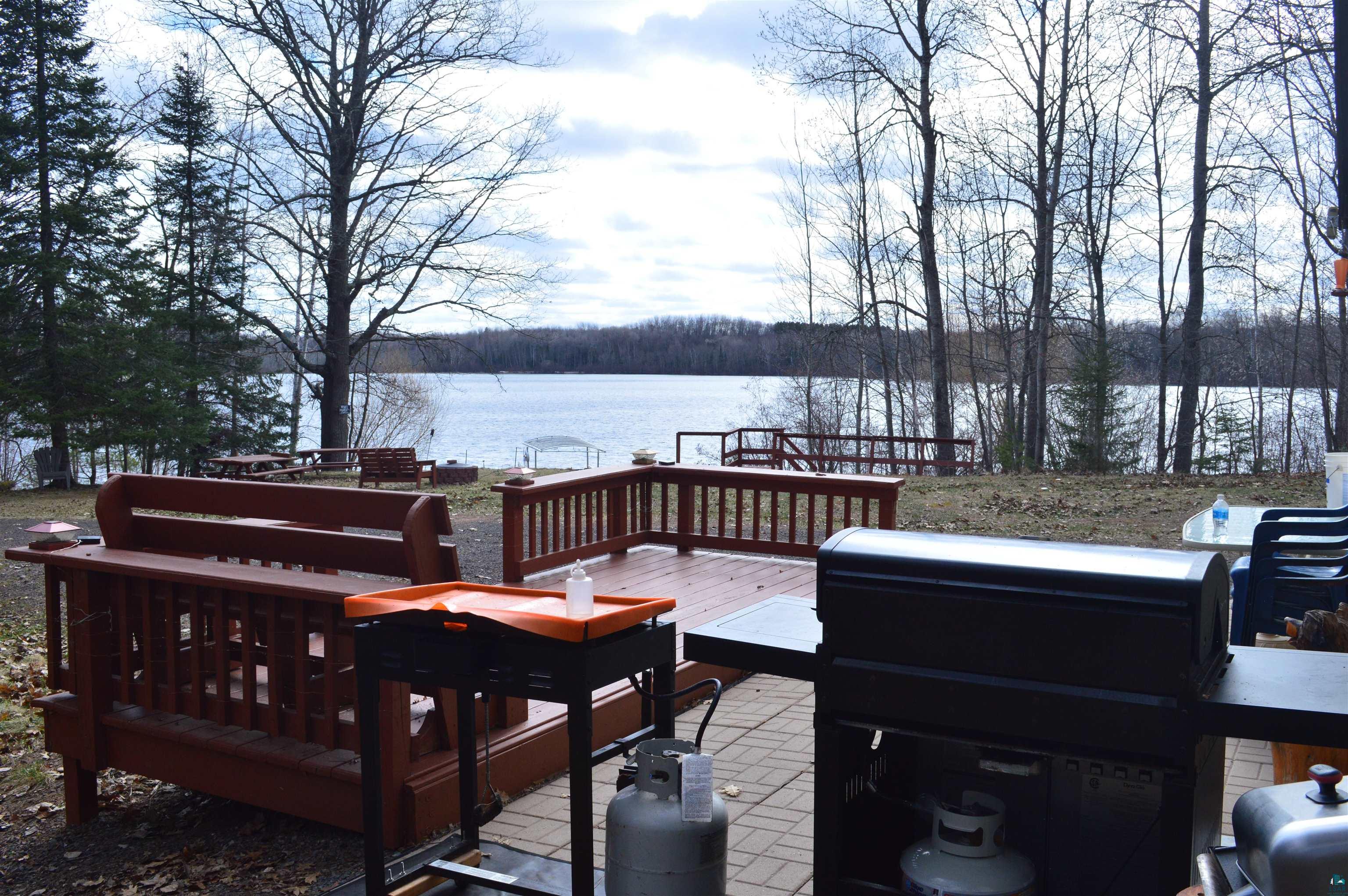 8467 County Rd P Lake Nebagamon, WI 54849 - Photo 15 of 25 Expansive waterfront setting featuring a wooden deck with railing, a stone paver patio, a treed perimeter, and a serene body of water