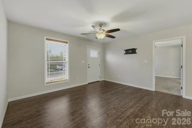 a view of an empty room with wooden floor and a ceiling fan