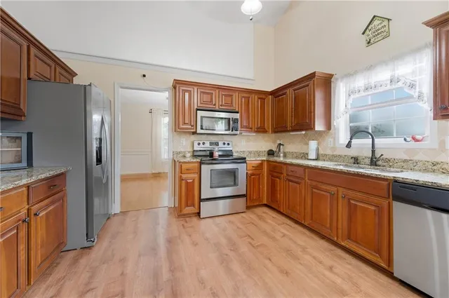 a kitchen with stainless steel appliances granite countertop a refrigerator a sink dishwasher a stove with wooden cabinets and floor