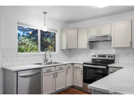 a view of an empty room with window and kitchen view