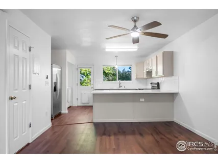 a view of an empty room and a kitchen with wooden floor