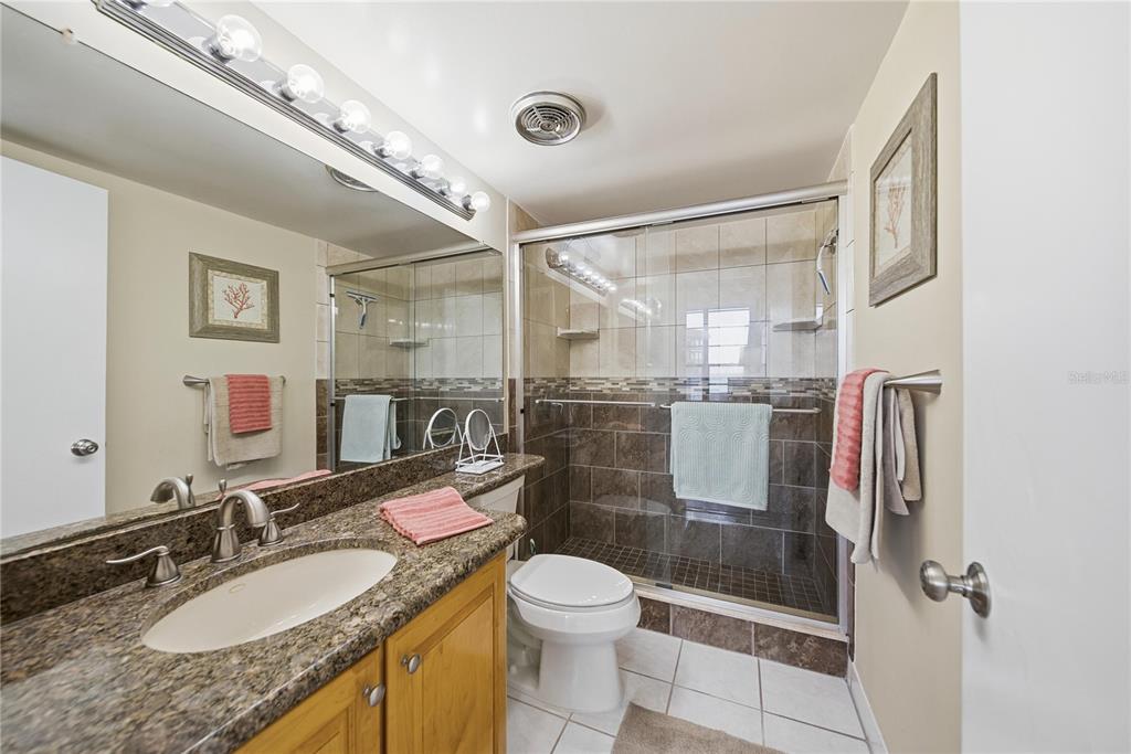 17580 Gulf Boulevard, Unit 302 Redington Shores, FL 33708 - Photo 20 of 37 a bathroom with a granite countertop sink a toilet a mirror and shower