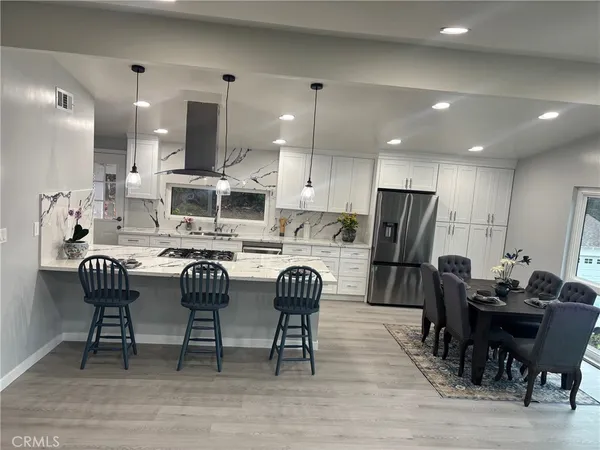 a kitchen with stainless steel appliances kitchen island granite countertop a dining table chairs refrigerator sink and cabinets