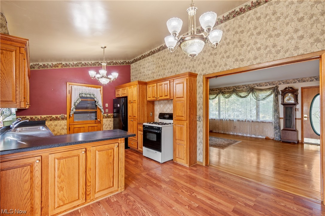 120 Lester Road New Franklin, OH 44319 - Photo 5 of 24 Kitchen featuring a high ceiling, a chandelier, dark countertops, brown cabinets, vaulted ceiling, white range with gas stovetop, light hardwood floors, and black refrigerator