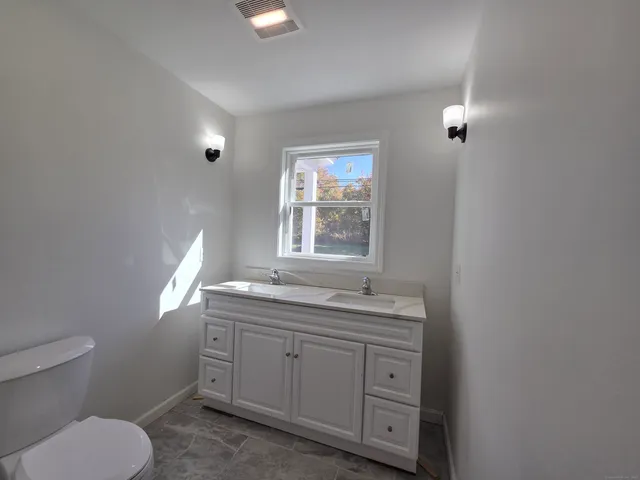 a bathroom with a granite countertop toilet a sink and a window