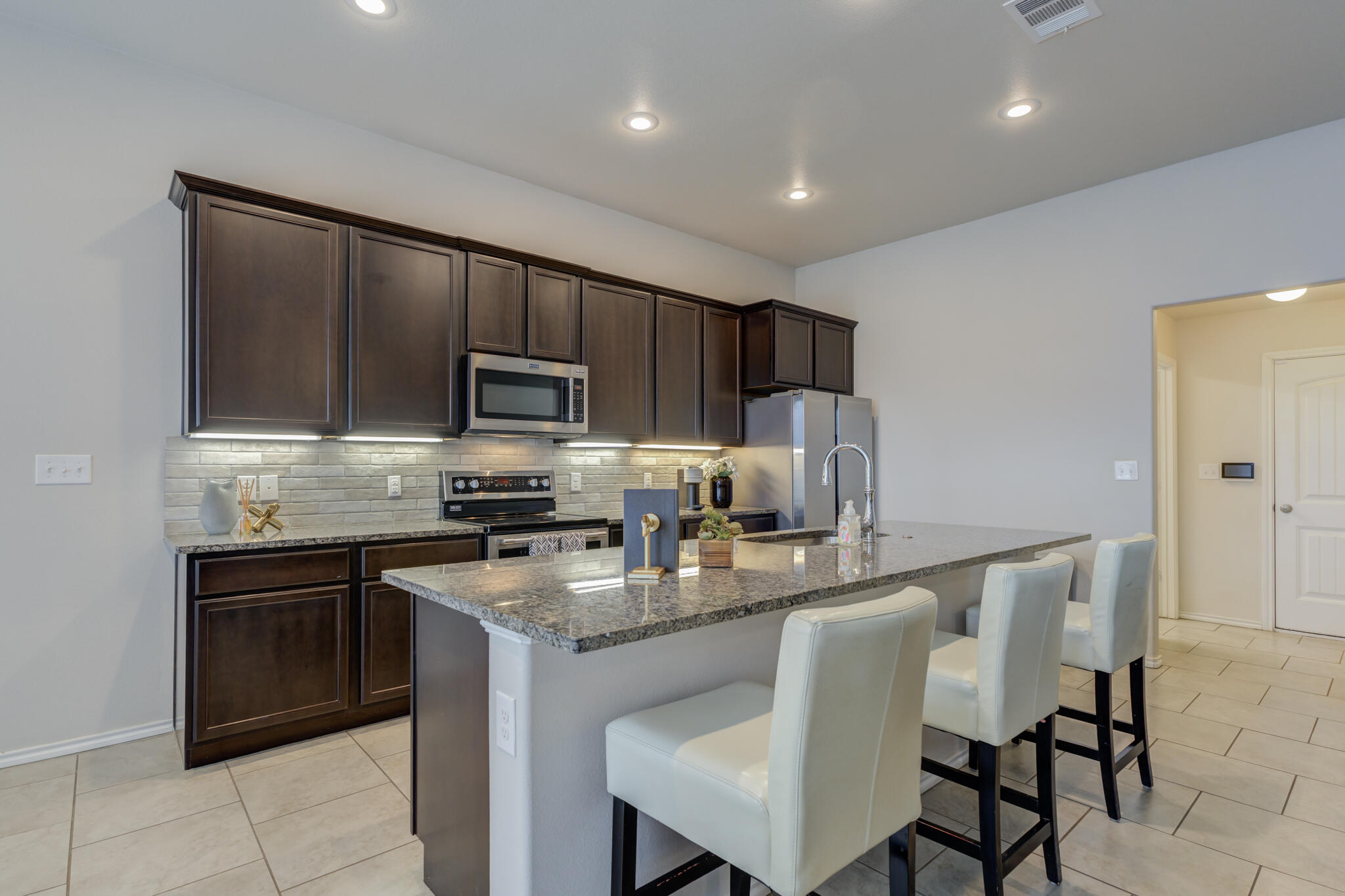 7201 94th Street Lubbock, TX 79424 - Photo 11 of 34 a kitchen with kitchen island granite countertop wooden cabinets a stove a microwave a island with a dining table and chairs