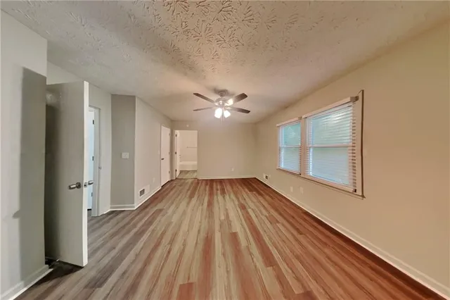 a view of a livingroom with wooden floor a ceiling fan and windows