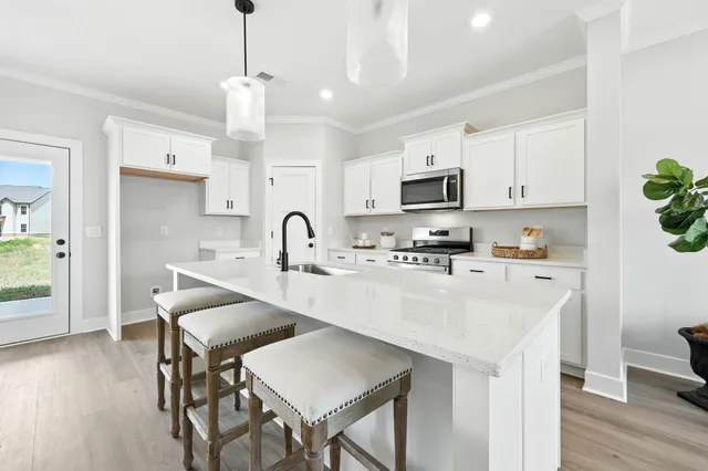 a kitchen with stainless steel appliances a stove a sink a microwave a refrigerator and white cabinets with wooden floor