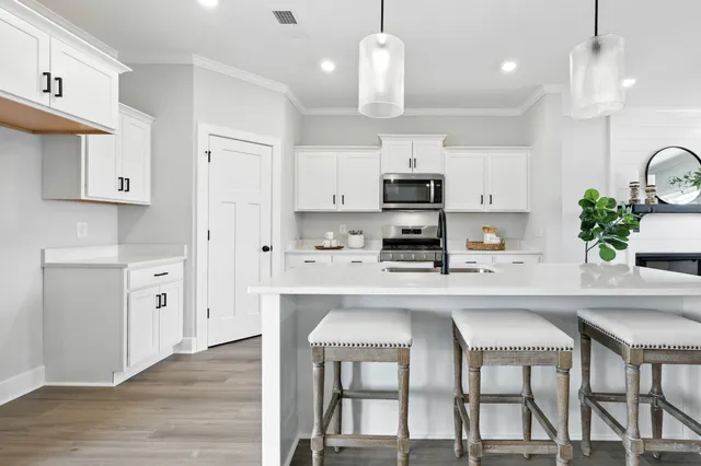 a kitchen with stainless steel appliances kitchen island granite countertop a sink a stove a refrigerator and white cabinets with wooden floor