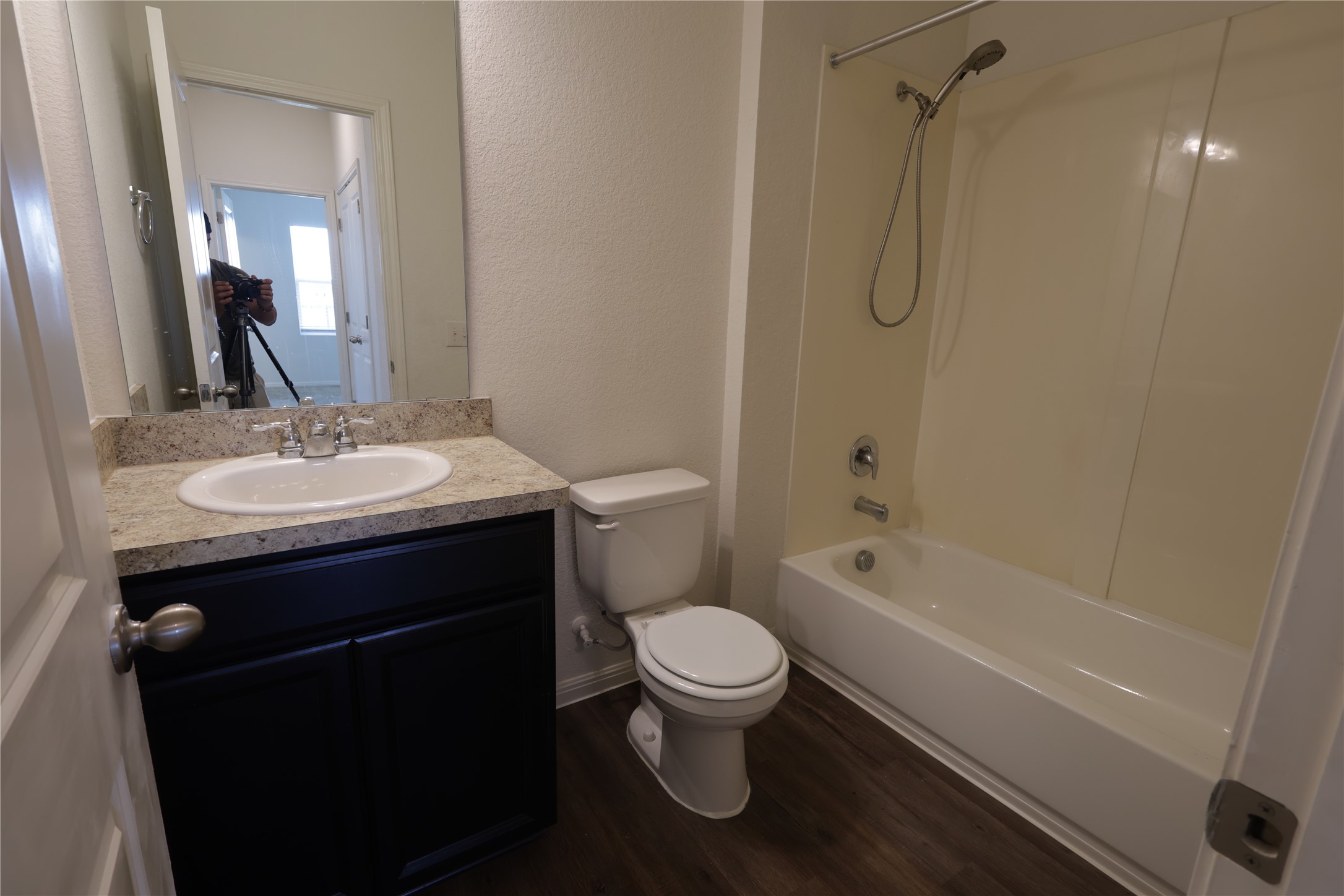 250 Seneca Loop Kyle, TX 78640 - Photo 7 of 22 A pristine bathroom features a single vanity, a toilet, and a combined shower-bathtub unit, all against dark wood flooring.