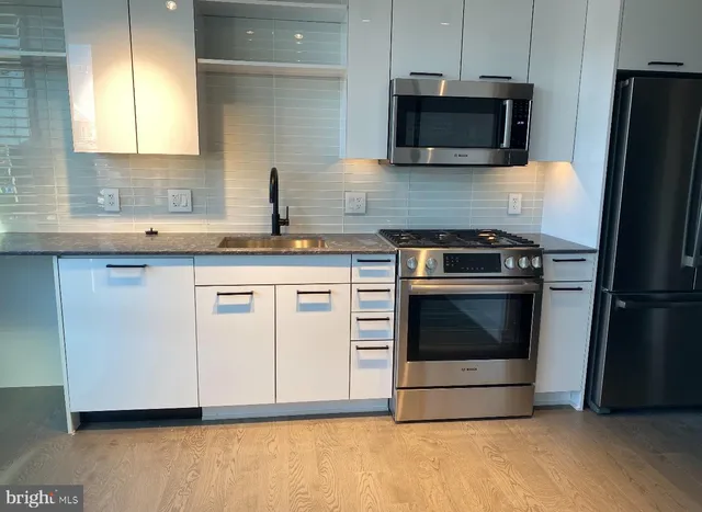 a kitchen with granite countertop a stove a microwave a refrigerator a sink and cabinets