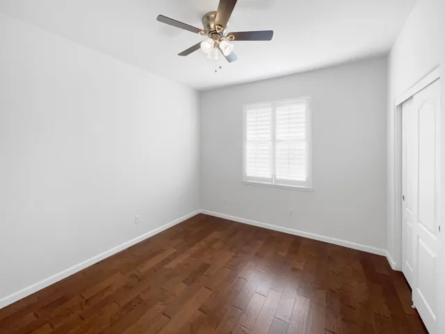 an empty room with wooden floor fan and windows