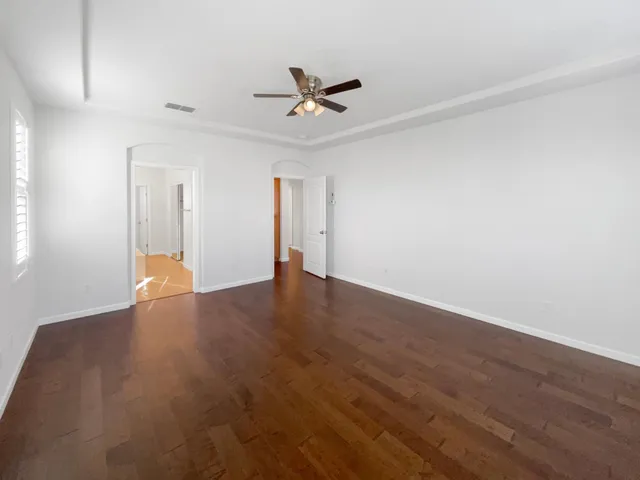 a view of an empty room with wooden floor and a ceiling fan