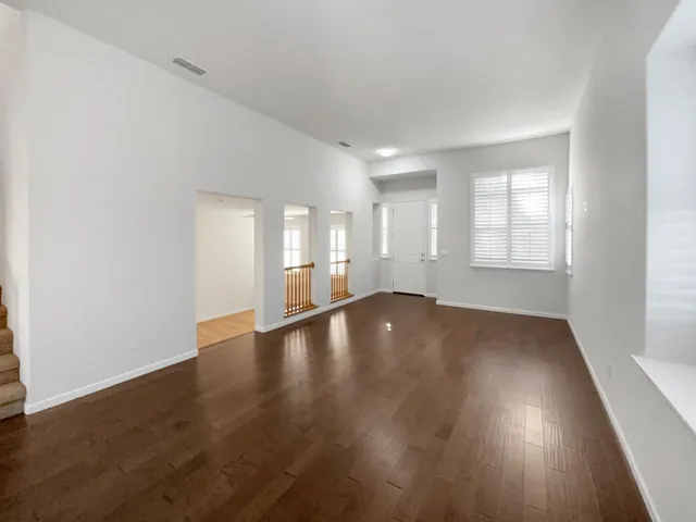 an empty room with wooden floor and windows with curtains