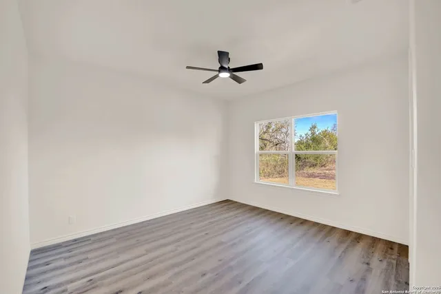 an empty room with wooden floor ceiling fan and windows