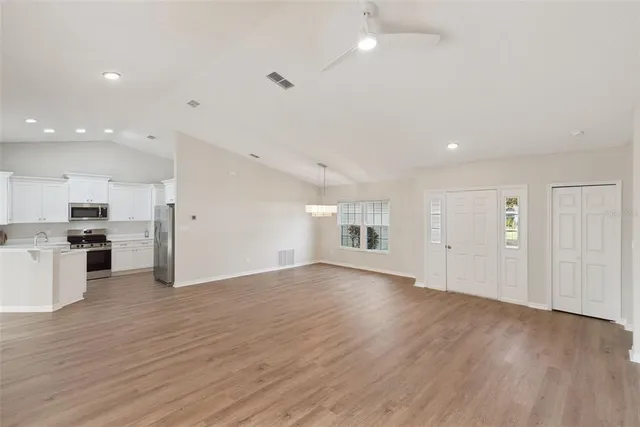 an empty room with wooden floor kitchen view and a window