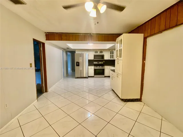 a view of a refrigerator in kitchen and an empty room