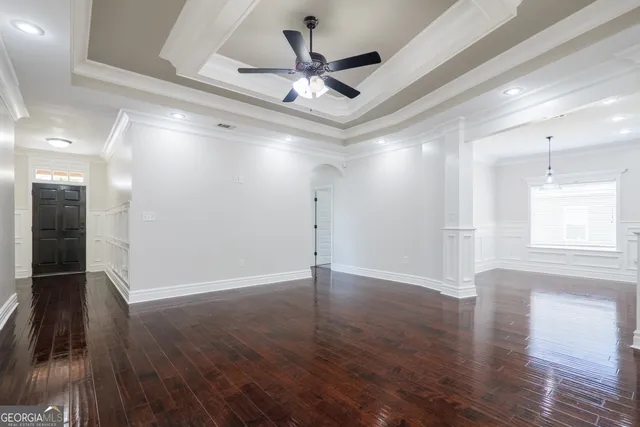 a view of an empty room with wooden floor and a ceiling fan