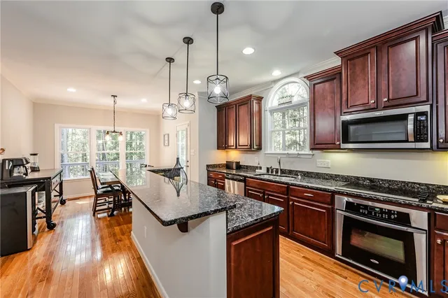 a kitchen with stainless steel appliances granite countertop a stove top oven a sink dishwasher a dining table and chairs with wooden floor