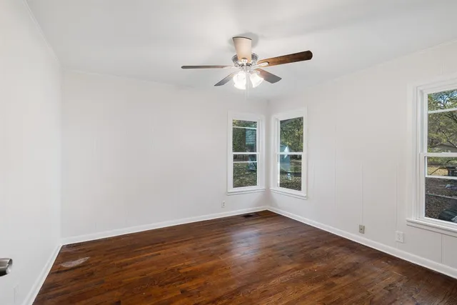 an empty room with wooden floor fan and windows