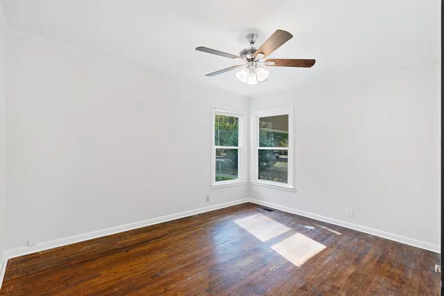 an empty room with wooden floor fan and windows