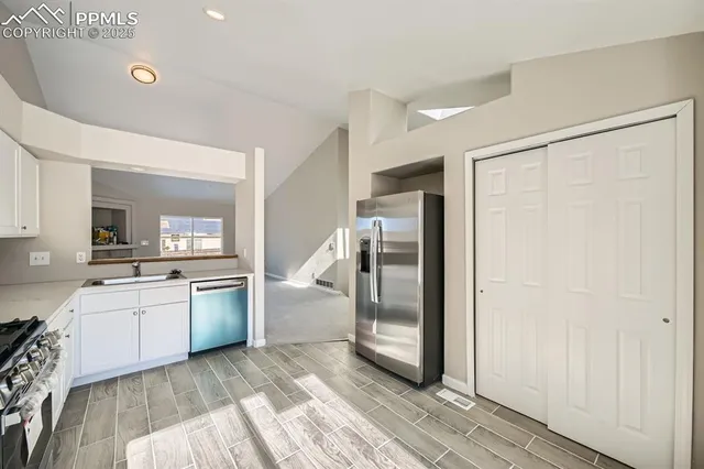 a kitchen with stainless steel appliances granite countertop a refrigerator a sink and white cabinets with wooden floor