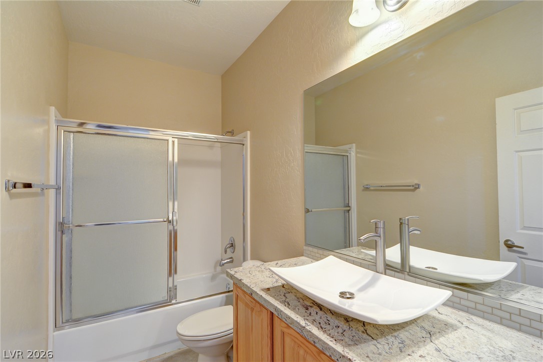 2339 Tranquil Moon Street Henderson, NV 89044 - Photo 12 of 15 A vessel sink rests on stone countertops alongside a classic shower and tub combination.