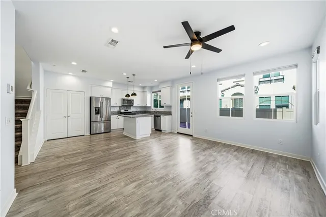 a living room with stainless steel appliances kitchen island hardwood floor and a ceiling fan