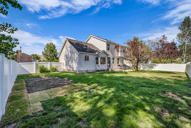 1147 West State Road Lehi, UT 84043 - Photo 29 of 31 Spacious backyard featuring a substantial lawn area, white vinyl fencing, mature trees, and a sunroom extension