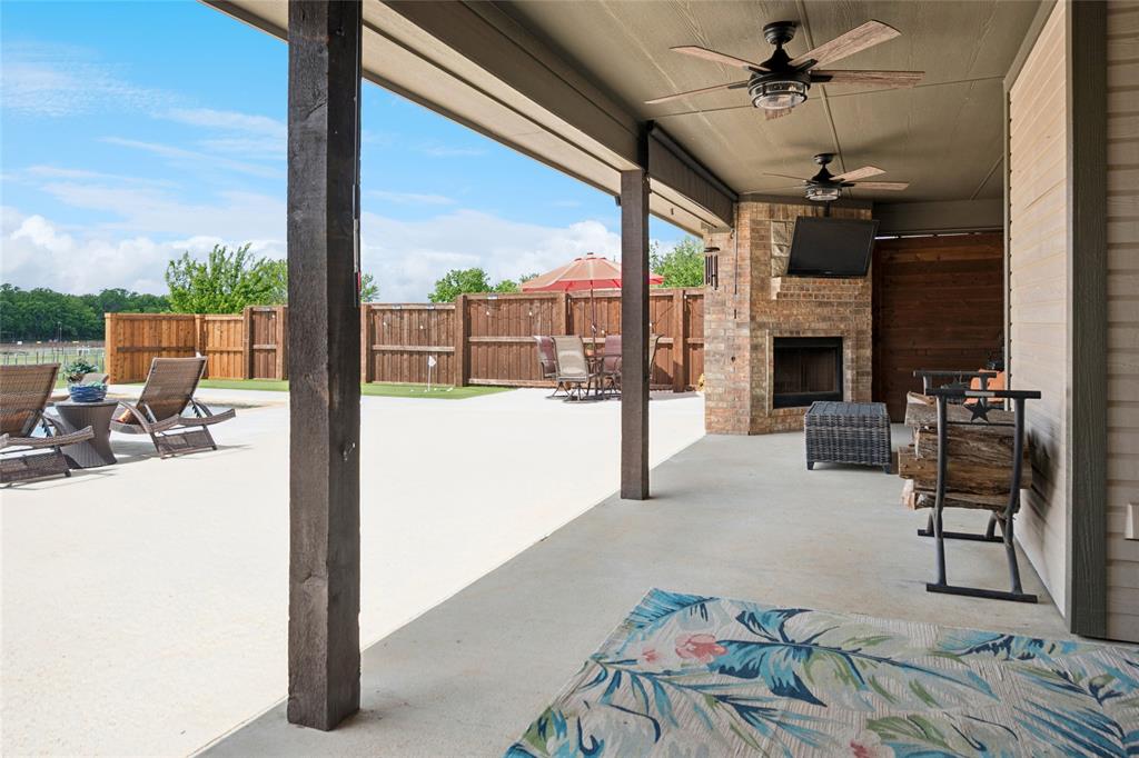 199 Newfield Lane Springtown, TX 76082 - Photo 30 of 38 Expansive covered patio featuring a brick fireplace, ceiling fans, and concrete flooring, with putting green adjacent to the pool.